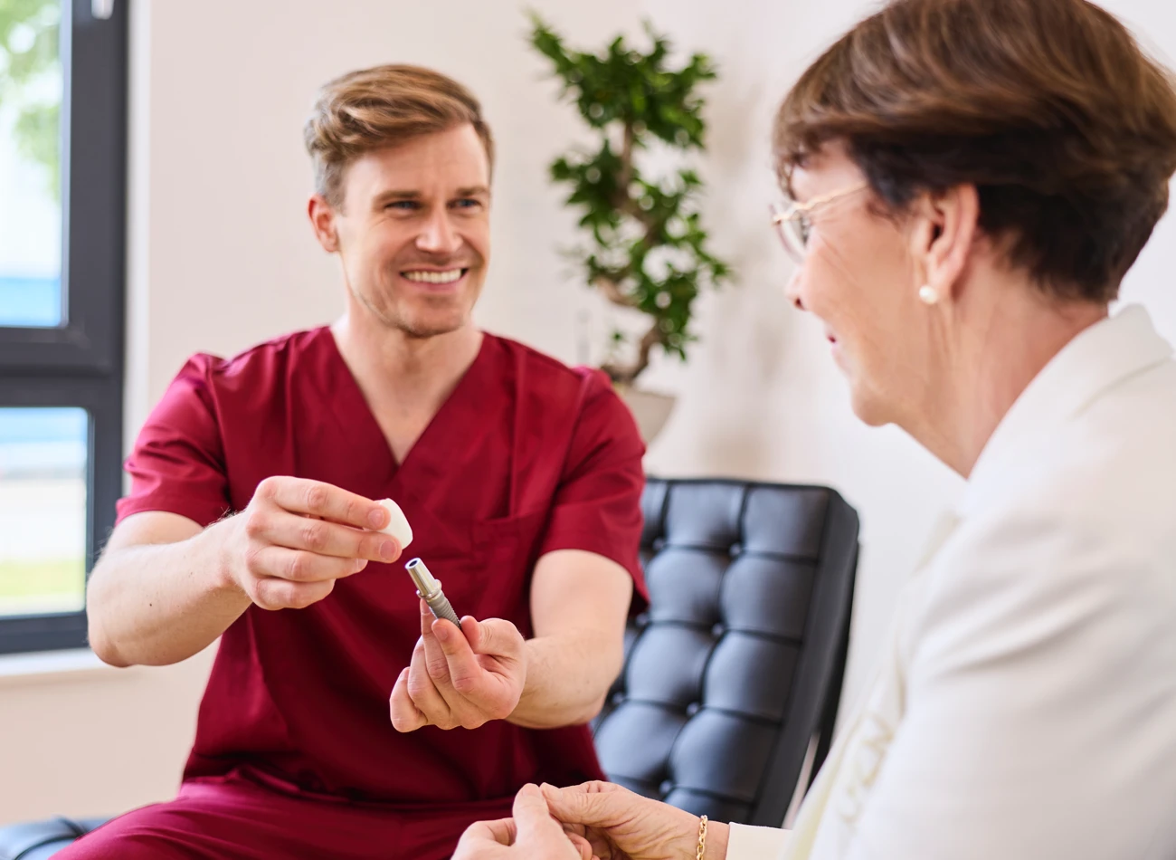 Fachzahnarzt Philipp Deuringer berät Patientin zum Thema Implantologie. Er zeigt ihr wie ein Implantat aussieht und funktioniert.