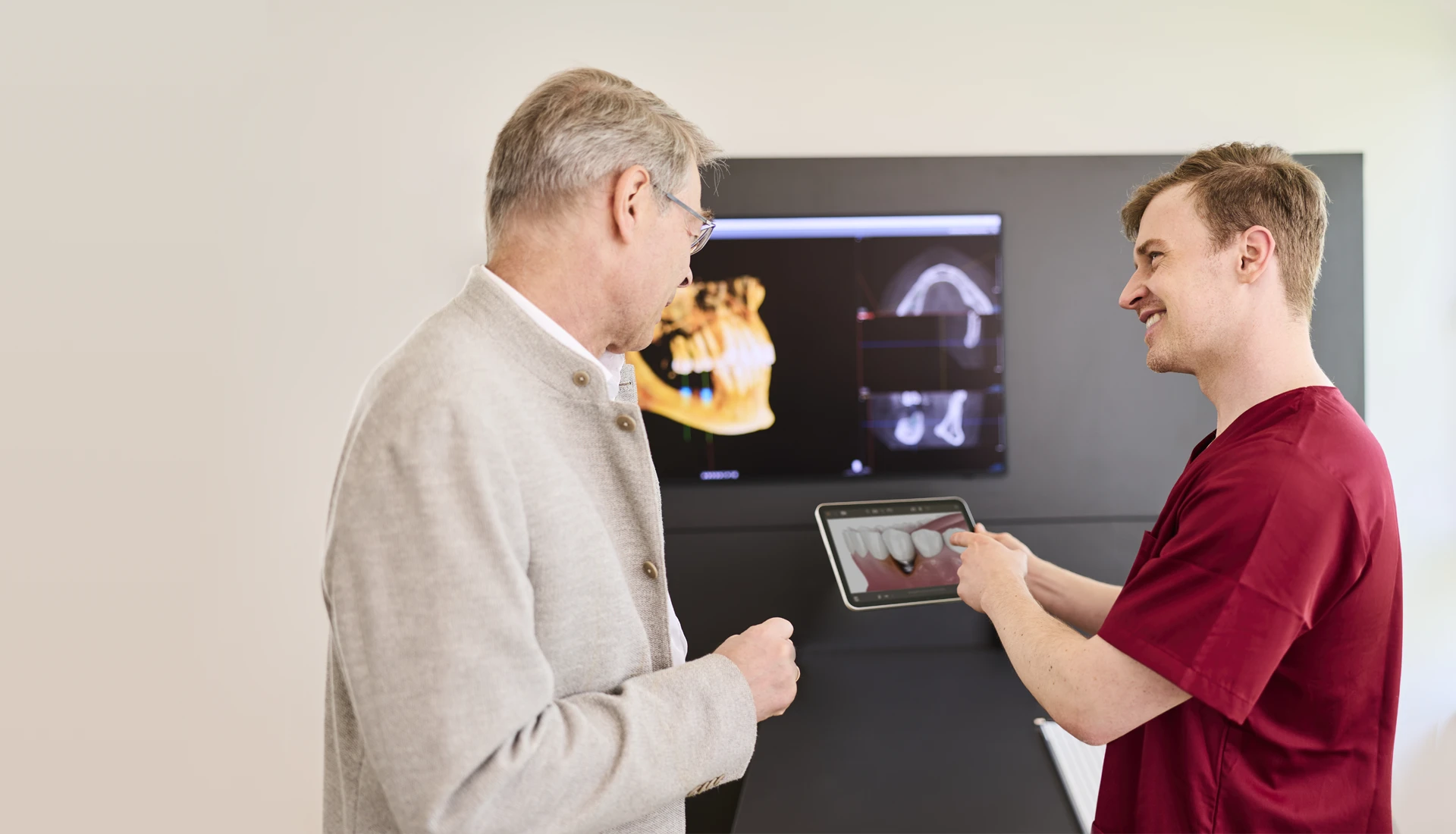 Fachzahnarzt Philipp Deuringer bespricht mit einem Patient am Tablet die Behandlung von Periimplantitis.